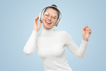 Young female enjoying favorite tracks via wireless headphones, dancing to music with happy face