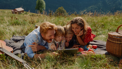 Family holding tablet picnic lying grass mountain hill. People using tab outdoor