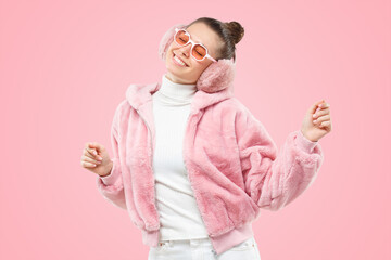 Happy smillig woman having fun dancing in pink fluffy bomber, colored eyewear and earmuffs
