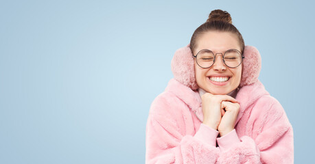 Banner of smiling girl in pink furry coat, earmuffs and glasses making wish with closed eyes