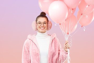 Girl celebrating her birthday, wearing pink fluffy coat and earmuffs, holding bunch of balloons