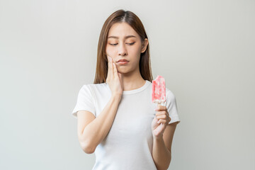 Face expression suffering from sensitive teeth and cold, asian young woman, girl hand touching her cheek, feeling hurt, pain eating ice cream, lolly. Toothache molar tooth at home, dental problem.