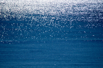 Abstract background. Spots of white reflections of shining sun on blue surface of sea waves. Sea on...