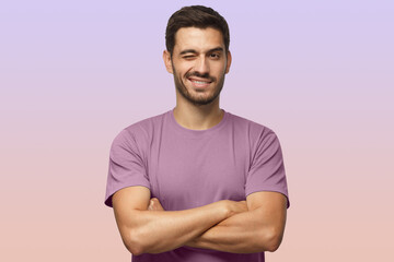 Handsome young man in t-shirt, with crossed arms smiling and winking, looking at camera