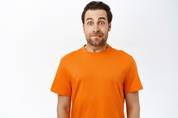 Image of guy looks with tempted, excited face, raising eyebrows up, standing in orange tshirt,...