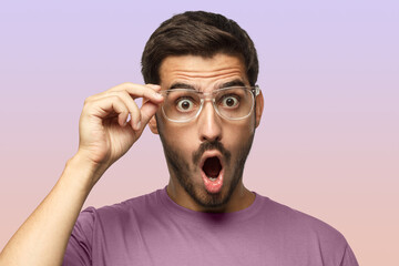 Studio portrait of young european man holding transparent plastic glasses looking with surprise