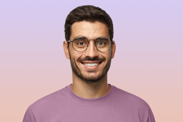 Close up shot of smiling attractive man in t-shirt and trendy round eyeglasses isolated on purple