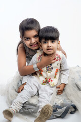 Cute little Indian asian siblings standing and embracing each other in white clothes ethnic standing against white background.