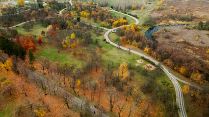 Autumn city park. Trees with colorful leaves. A cycle path winds between the trees. Autumn landscape. Aerial photography.