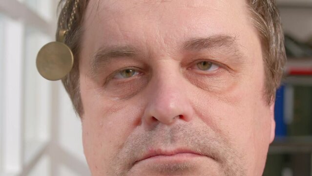 Portrait of man falls asleep in hypnosis session. Human eyes follow swinging hypnotic pendant on chain and close.