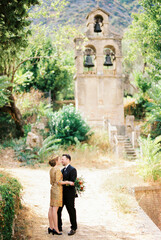 Fototapeta na wymiar Groom hugs bride near the ancient bell tower in the park