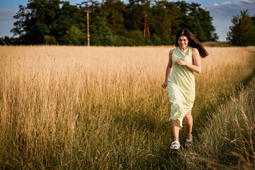 a beautiful girl with long dark hair in a light green dress runs through a field on a summer evening