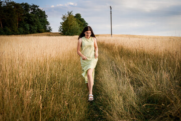 a beautiful girl with long dark hair in a light green dress runs through a field on a summer evening