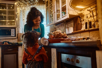 Happy black mother and daughter preparing Thanksgiving turkey in kitchen.