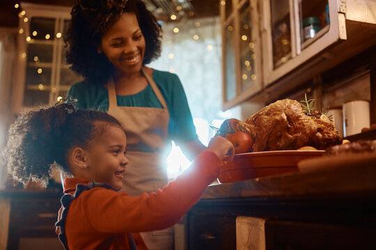 Happy black little girl decorating Thanksgiving turkey with her mother in kitchen.