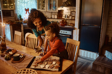African American little girl and her mother baking Christmas cookies in kitchen.