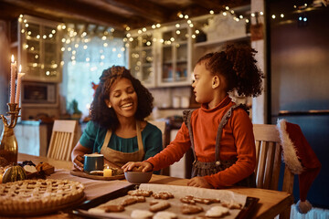 Fototapeta na wymiar Black little girl assisting her mother in making gingerbread cookies for holidays in kitchen.