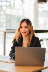 Asian businesswoman sitting at work using a calculator to calculate analytical statistics front view of beautiful woman holding pen and graph paper with laptop on desk in office