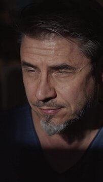 Portrait of a good looking man in a dark room leaning forward into the light looking away and smiling and leaning back to the dark at the end. High quality 4K video footage.