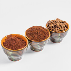 three small saucers with coffee beans, ground coffee and cocoa on a white background.