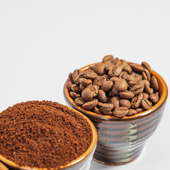 Cups with roasted coffee beans and ground coffee, white background and copy space.