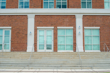 Concrete steps lead to a red double door of a historic building. The wall of the building is made...