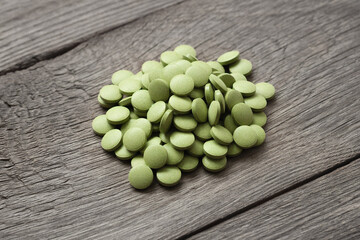 Lots of scattered green pills on a wood background, dietary supplements,.Chlorella pills, concept of superfood and detox