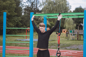 Fitness trainer exercises the upper half of the body in the morning on an outdoor workout court with the help of expanders and rubber bands. Trapezius, shoulder muscles workout