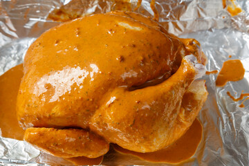 chicken carcass stuffed with pear in soy sauce with spices on foil ready for baking close-up.