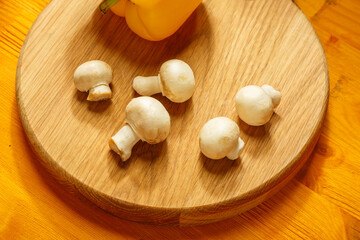 Champignon mushrooms, and yellow pepper on a round wooden board on the table.