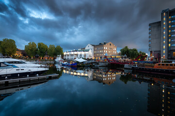 Fototapeta premium Boats in marina with restaurants and hotels in a modern city. London, United Kingdom. Travel Destination. Night after cloudy sunset.
