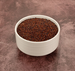 Side view of a white bowl filled with red quinoa on a maroon tabletop.