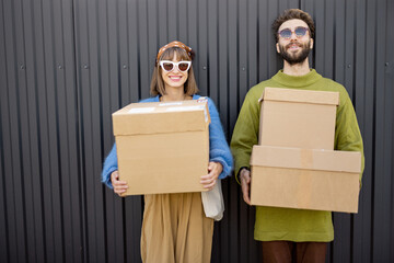 Portrait of young and stylish couple standing with cardboard parcels together outdoors. Concept of...