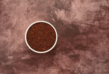 Top view of a white bowl filled with red quinoa offset on a maroon tabletop.