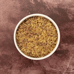 Top view of rice and lentils dry food mix in a white bowl atop a red mottled tabletop.