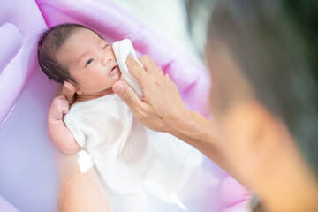 沐浴で顔を洗われる赤ちゃん（新生児・パパ・父・子供・子ども・0歳・育児・子育て・お風呂・入浴）