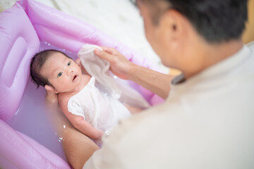 Fototapeta na wymiar 沐浴で顔を洗われる赤ちゃん（新生児・パパ・父・子供・子ども・0歳・育児・子育て・お風呂・入浴）