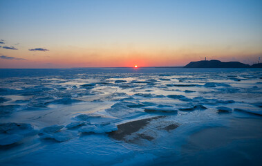 Aerial view of sunset over the frozen sea. Winter landscape on seashore during dusk. View from above of melting ice in ocean on sunrise with horizon. Global warming. Vivid colorful skyline scenics.