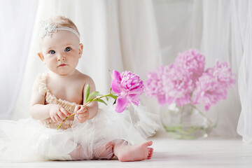 Little pretty girl with blue eyes sits on a floor with flowers of a peony. Copy space