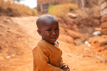 Portrait of a poor african child crying in the village, he wears dirty clothes.