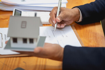 Accountant, businessman, real estate agent, businessman handing model house to customers along with house interest calculation documents for customers to sign.