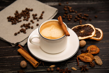 A mug of coffee on a wooden background with spices.