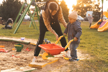 Mother and child playing with wheelbarrow in sandbox. Little builder. Education, and imagination, purposefulness concept. Support childhood parenthood symbol