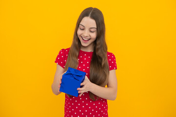 Amazed surprised emotions of young teenager girl. Child teen girl 12-14 years old with gift on yellow isolated background. Birthday, holiday present concept.