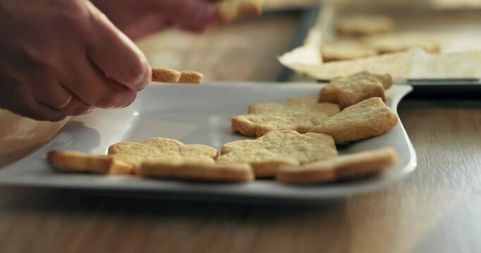 Selective focus close up shot on woman's hands putting cookiei different shapes from baking tray on white plate. Happy mother's day concept.