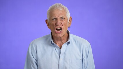 Frustrated elderly man in 70s, with anger talking, shaking head no, isolated on light purple background.