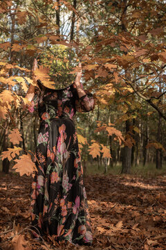 woman in long floral dress standing in autumn in the forest holding round mirror reflecting foliage in abstract portrait