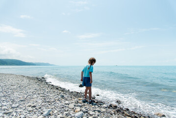 Fototapeta na wymiar Little cute girl sits on a pebble beach and plays with pebbles