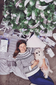 Vertical picture of a woman laying under the christmas tree with her dog