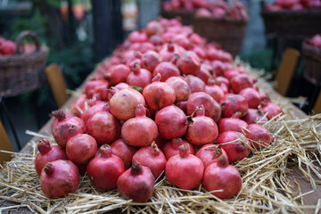 Harvest of ripe pomegranate on dry straw at outdoor farmers market in Tbilisi Georgia. Vegetarian healthy food